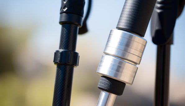 A close-up comparison of a carbon fiber and an aluminum trekking pole, shot in natural daylight with a shallow depth of field. The carbon pole has a sleek, matte black finish, while the aluminum pole has a brushed silver metallic look. The grips, tips, and adjustable mechanisms are clearly visible, highlighting the differences in construction and materials. The poles are angled slightly, creating a dynamic composition that emphasizes their weight, durability, and ergonomic design. The background is blurred, keeping the focus on the detailed, textural qualities of the poles themselves. A close-up comparison of a carbon fiber and an aluminum trekking pole, shot in natural daylight with a shallow depth of field. The carbon pole has a sleek, matte black finish, while the aluminum pole has a brushed silver metallic look. The grips, tips, and adjustable mechanisms are clearly visible, highlighting the differences in construction and materials. The poles are angled slightly, creating a dynamic composition that emphasizes their weight, durability, and ergonomic design. The background is blurred, keeping the focus on the detailed, textural qualities of the poles themselves.